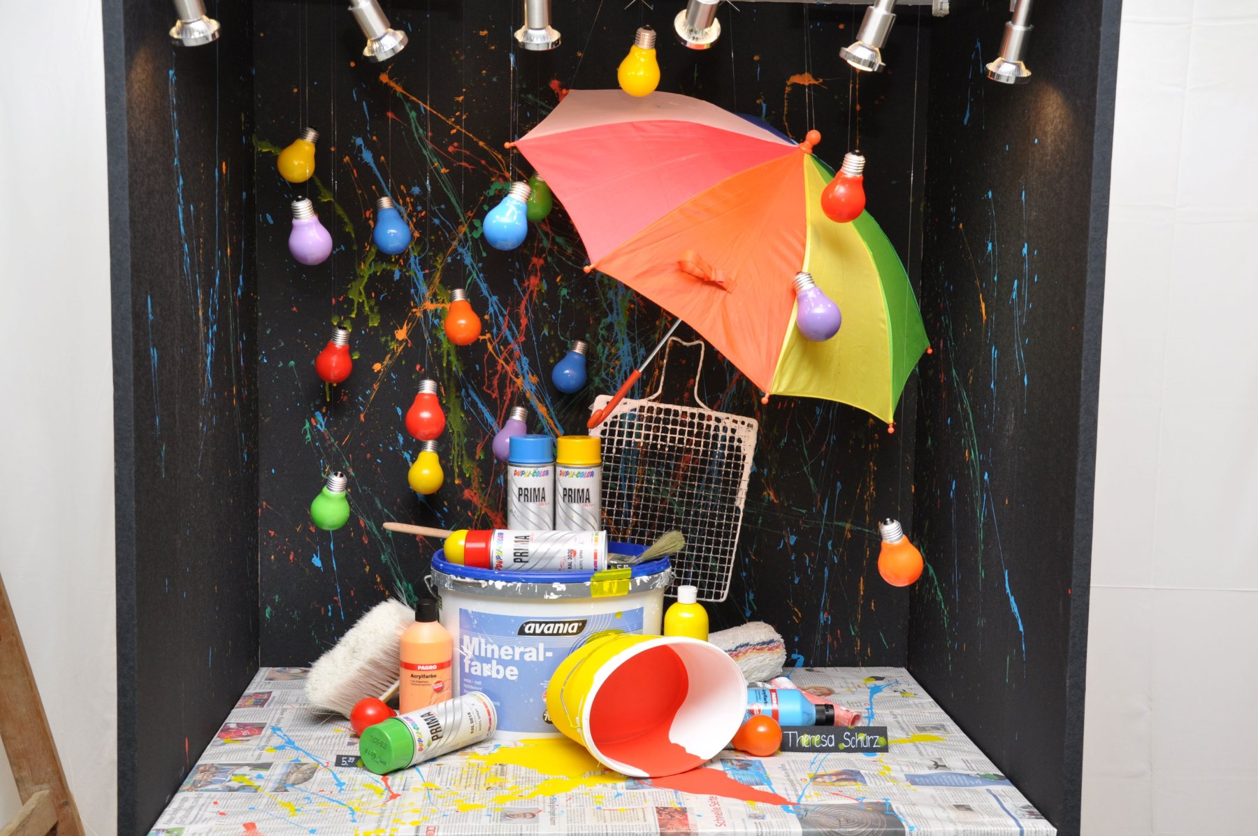 Schaufenster mit buntem Regenschirm, bunten Farbdosen, Malerzubehör und Glühbirnen