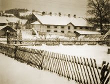 ein Wirtschaftsgebäude im Winter, mit Holzzaun im Vordergrund