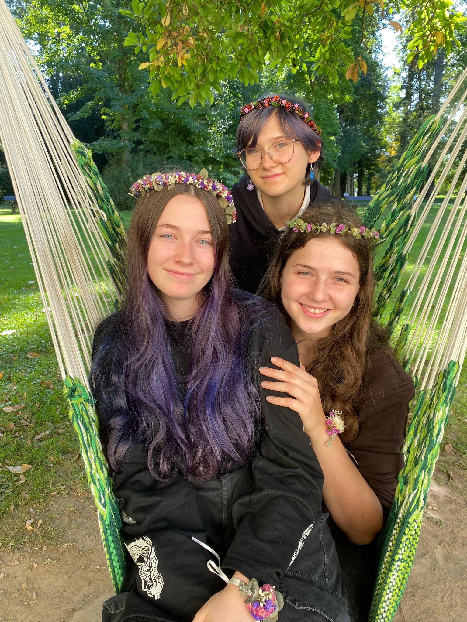 drei Mädchen mit Blumenkränzchen im Haar sitzen in einem Hängesessel