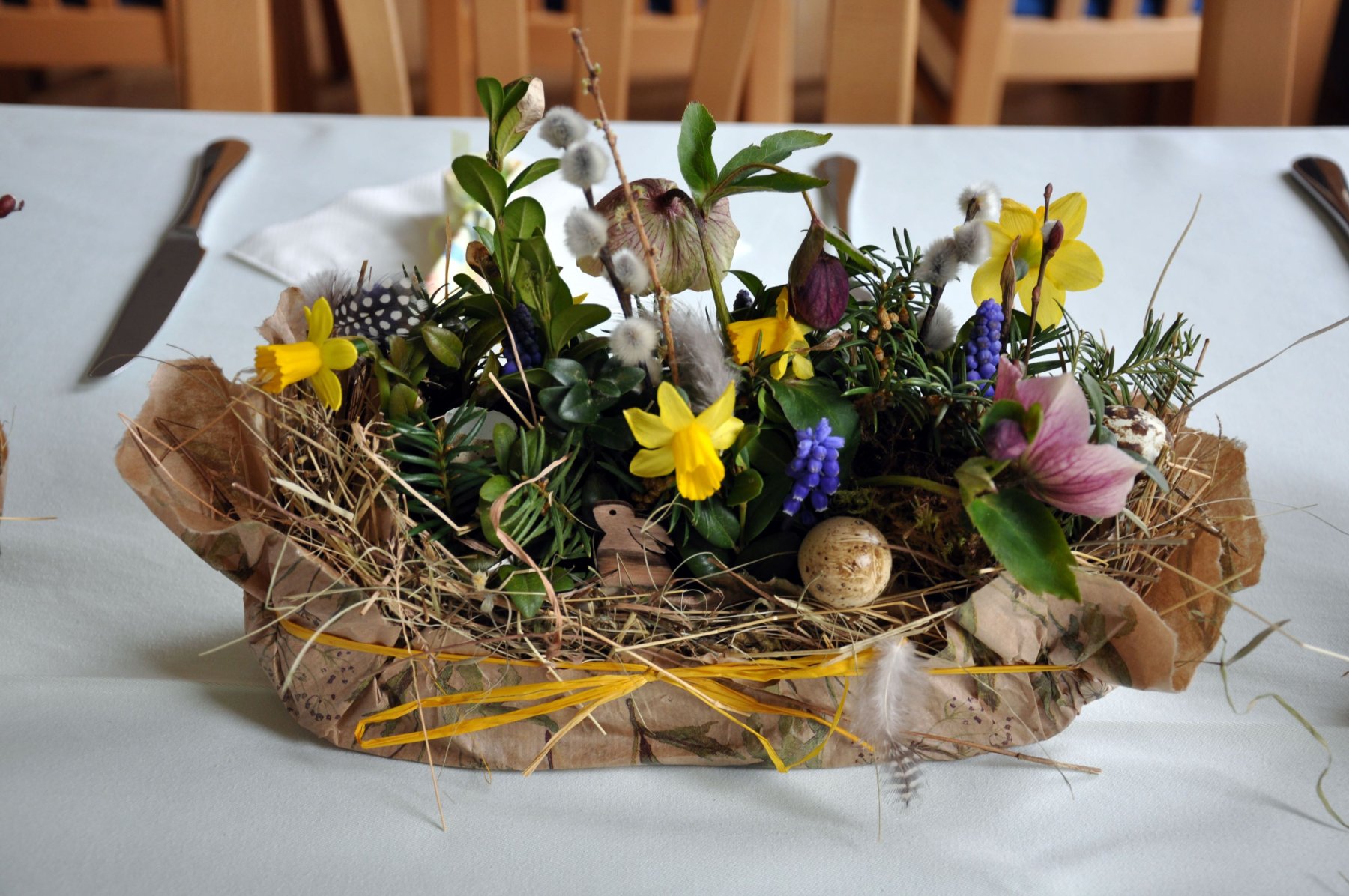 österlicher Tischschmuck mit gelben und violetten Frühlingsblühern, Palmkätzchen und Federn