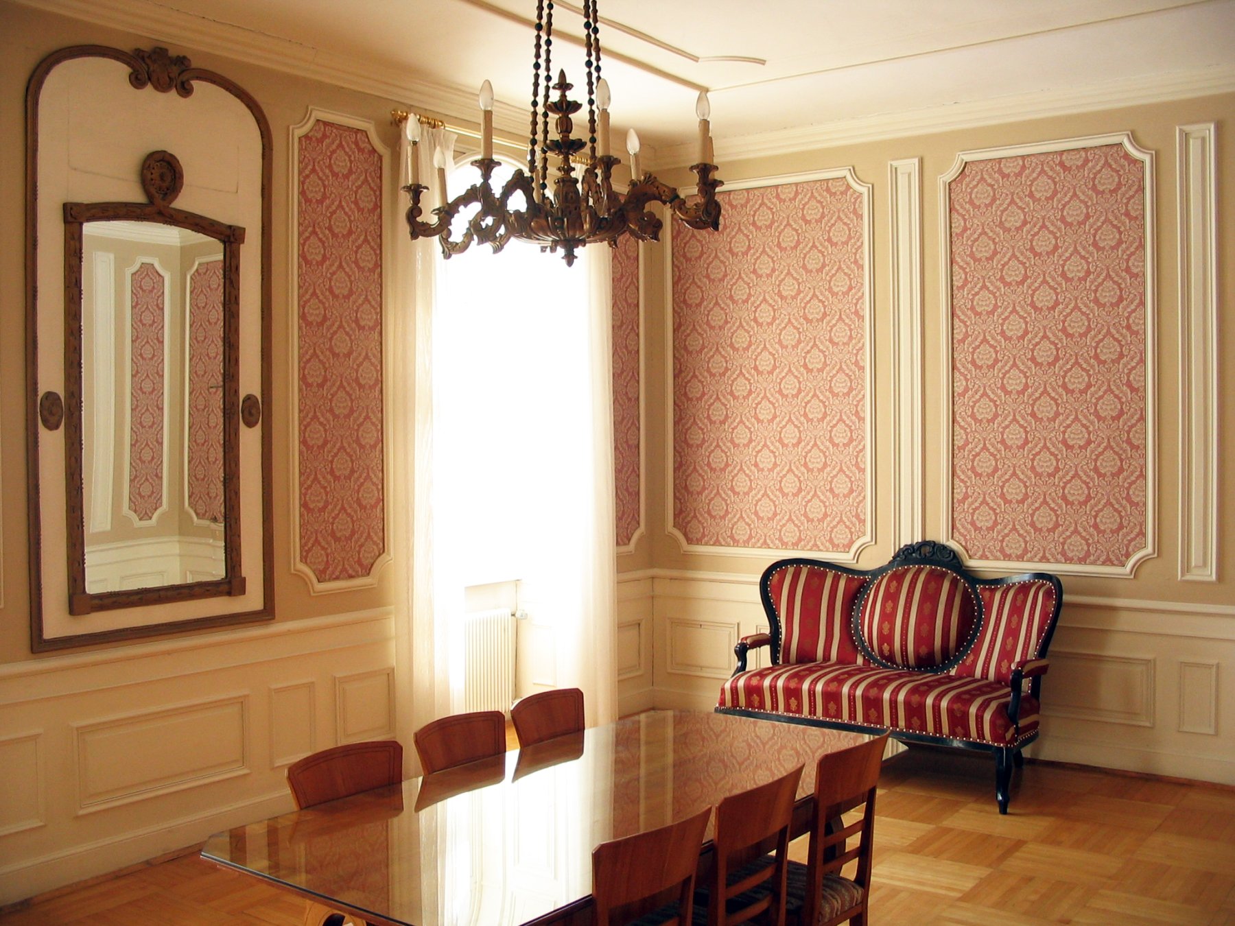 Raum mit Stuckarbeiten und rosa Wandtapete, im Hintergrund steht eine antike Couch